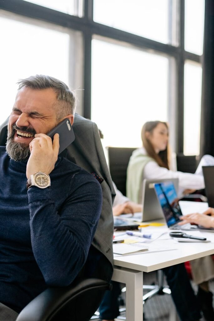 Middle-aged businessman enjoys a phone call in a lively office setting.